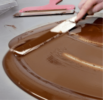 During tempering, the crystallisation of the cocoa butter within the chocolate liquid is achieved. Tempering allows you to solidify chocolate in a way that keeps it glossy, causes it to break with a distinctive snap